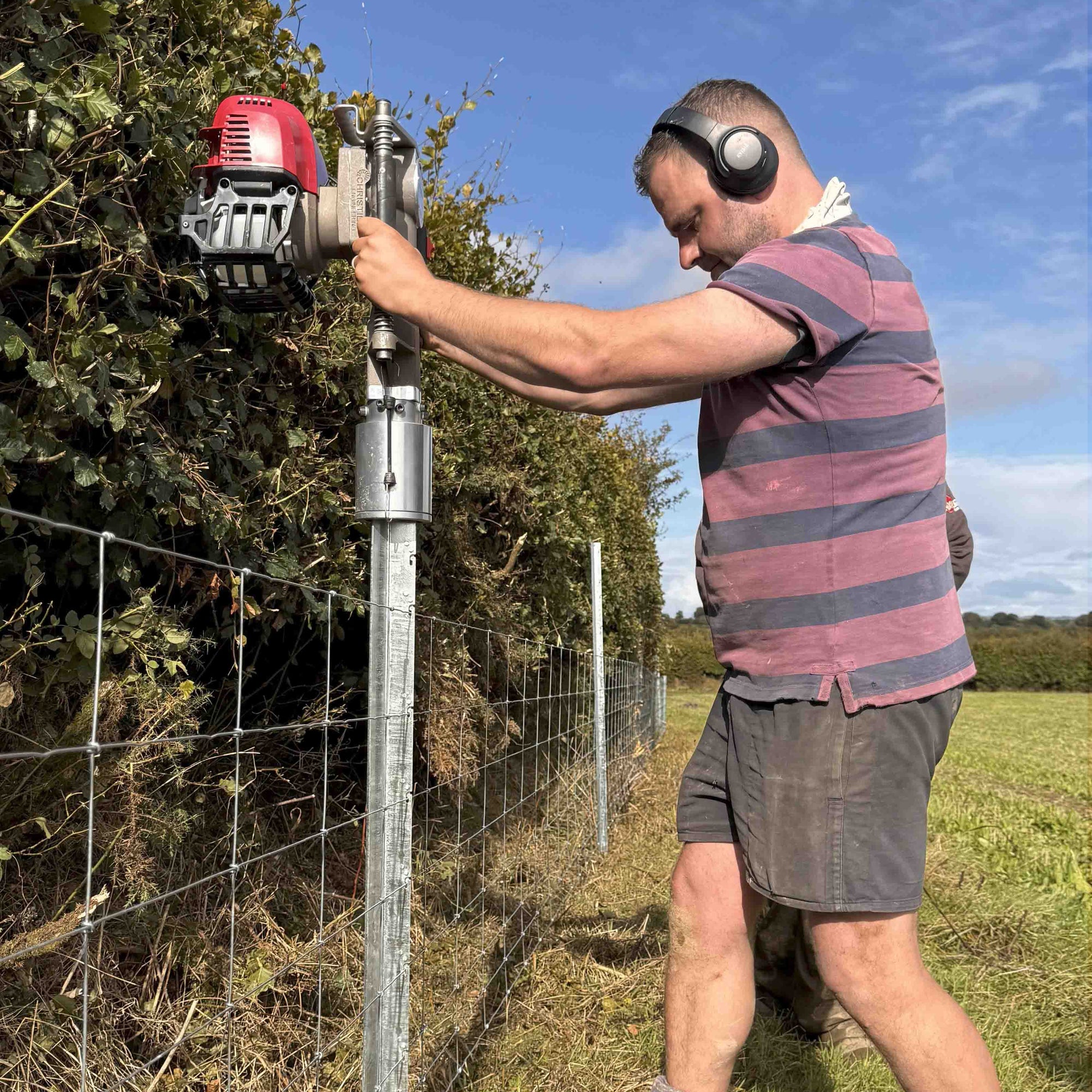 Person using a post driver on a clipex fence in an outdoor setting