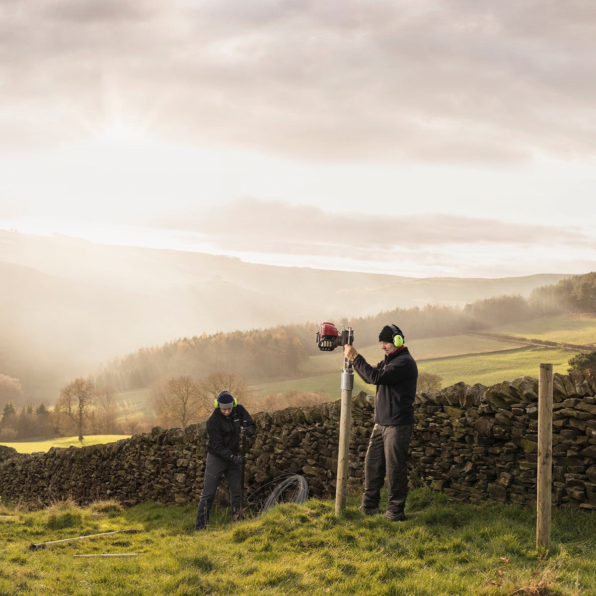 Farm contractors installing a 4&quot; timber fence along a stone wall