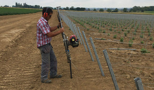 Post driver being used to install ground anchors in a vineyard
